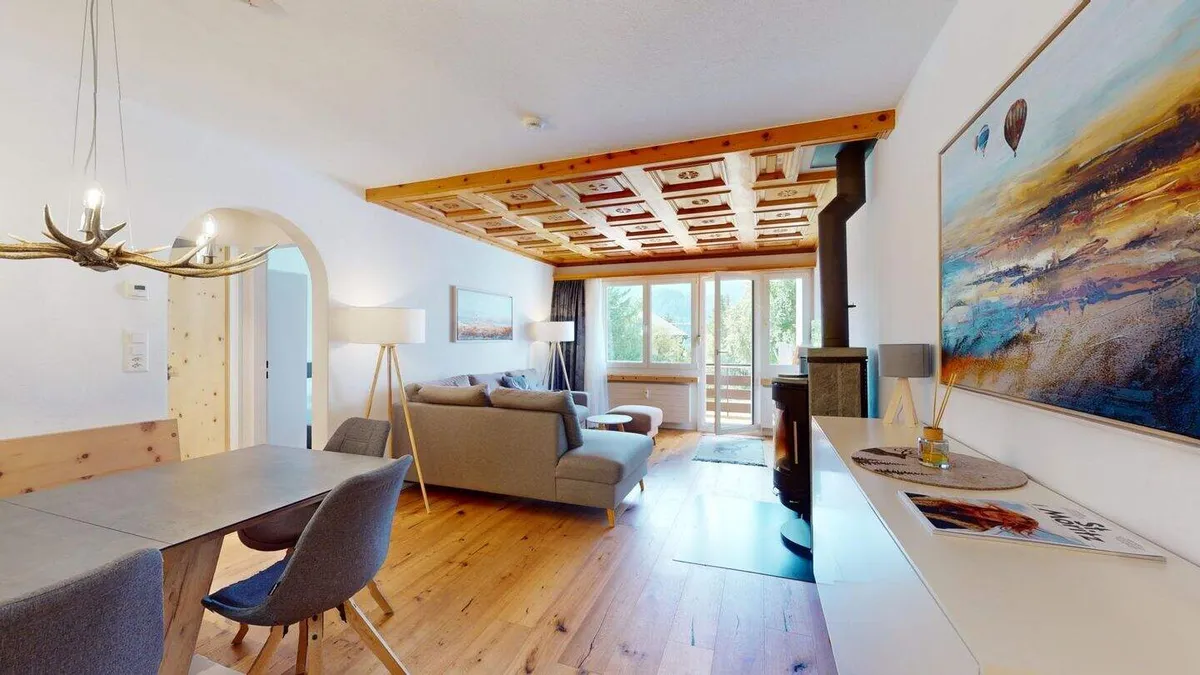 Blick vom Essbereich ins Wohnzimmer mit Ofen und grossem Landschaftsbild