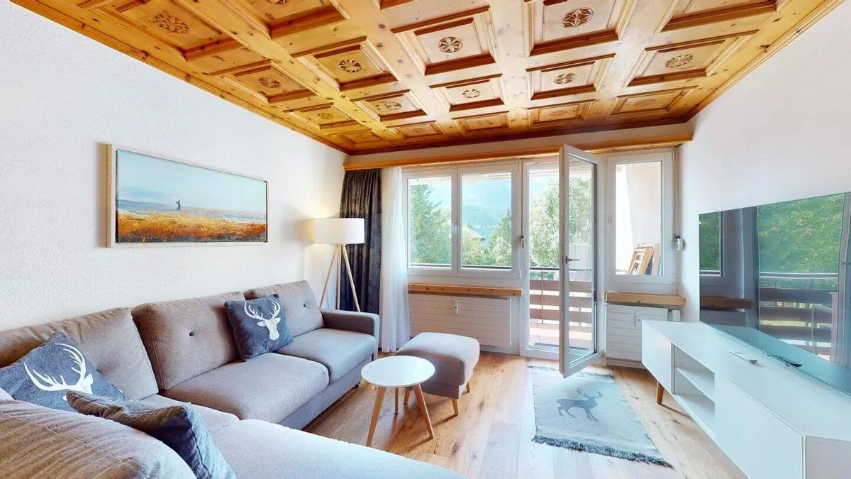 Wohnzimmer mit Sofa und Balkontür, durch das Fenster Blick auf die Berge