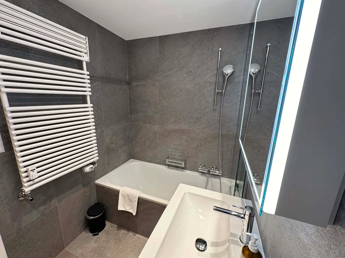 Renoviertes Badezimmer mit Badewanne, Duschbrause und Handtuchheizkörper