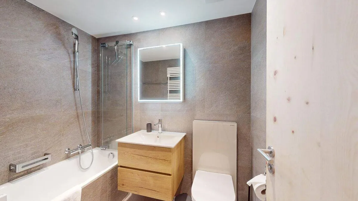 Badezimmer mit Badewanne, Lavabo und beleuchtetem Spiegel