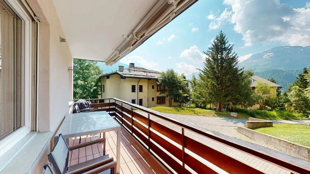 Sonniger Balkon mit Blick auf Garten, Tannen und Berge