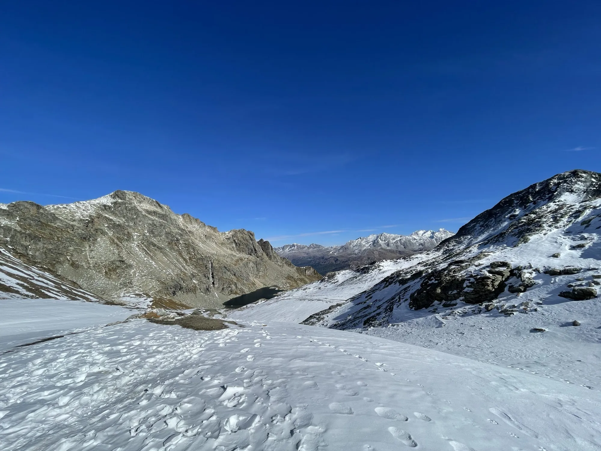 Lunghinsee mit Schneeresten vor Bergen unter blauem Himmel