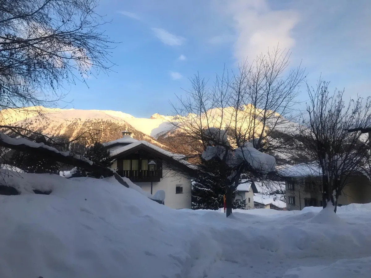 Verschneite Häuser im Abendlicht vor der Bergkette